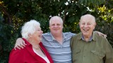 Male NDIS client smiling with his arms over his parents' shoulders